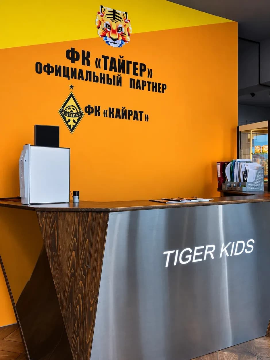 Стойка ресепшн Tiger Kids и стена с эмблемами ФК «Тайгер» и ФК «Кайрат»